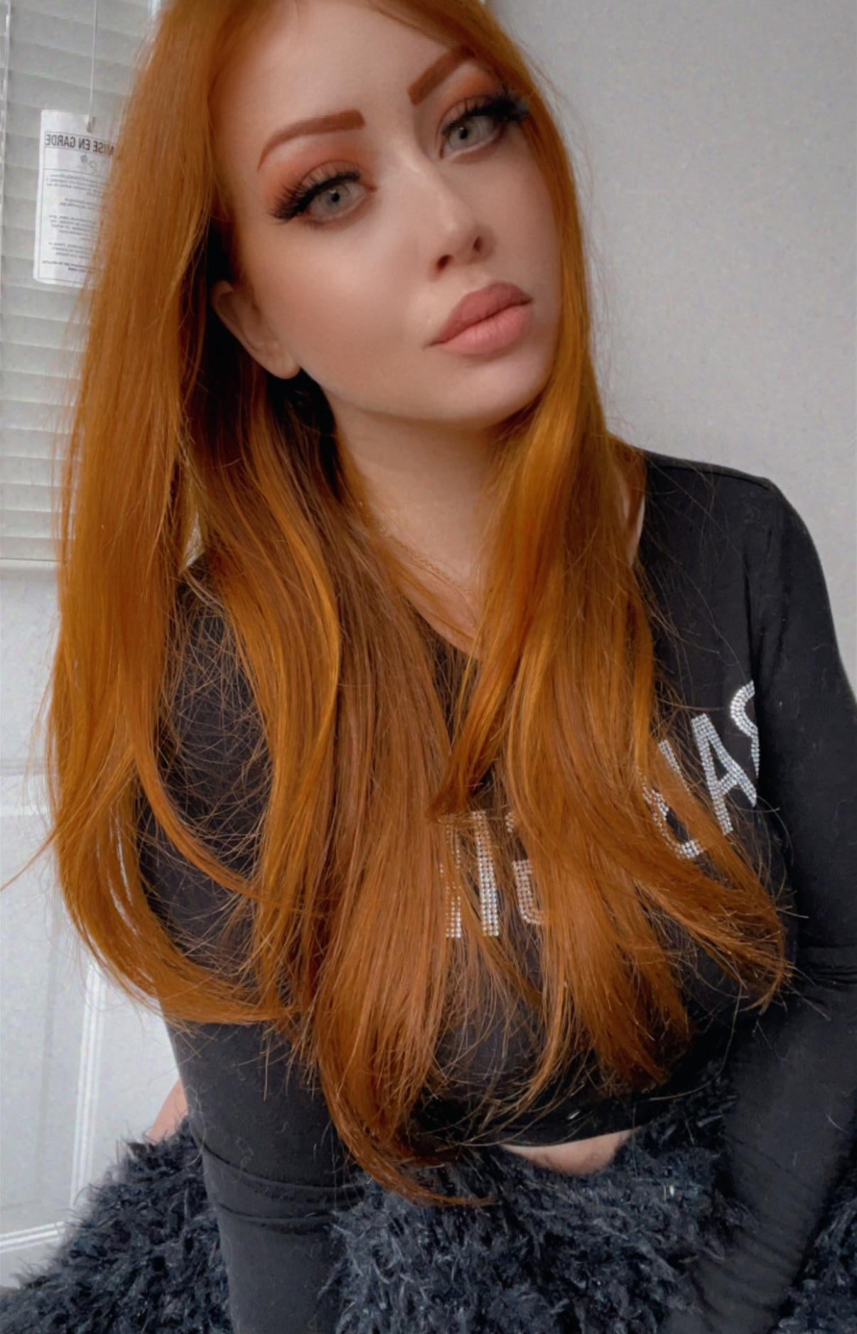 Redhead girl flaunts smooth-shaven intimate area and alluring breasts in selfie.